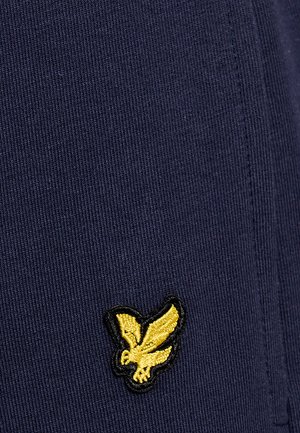 Gele geborduurde adelaarlogo op donker marineblauw geribbelde stof met zichtbare naden.