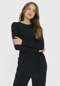 Čierny dlhý rukáv top z lesklého materiálu s okrúhlym výstrihom. Strih je priliehavý, s hladkou textúrou a minimálnymi dizajnovými detailmi.