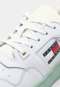 Baskets blanches en cuir avec une languette texturée, des détails perforés et une semelle en caoutchouc vert menthe. Présentant une étiquette de marque multicolore.