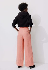 Pantalons larges roses, en tissu texturé, taille haute et poches arrière. Associés à un sweat à capuche noir. Design simple et décontracté.