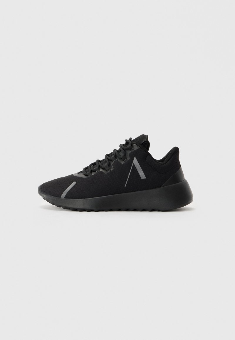 Zapatilla deportiva negra con suela gruesa, parte delantera con cordones y detalle de franja reflectante en ángulo en el costado y la zona de los dedos.