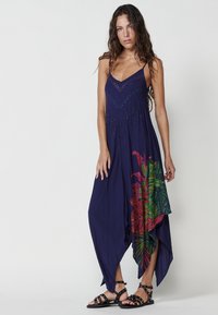 Robe maxi bleu marine avec un décolleté en V plongeant et des détails en perles délicats. Présente un imprimé tropical coloré sur le côté et un ourlet asymétrique.