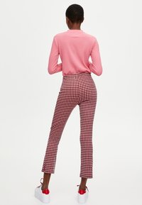 Dopasowany różowy prążkowany top z długim rękawem w połączeniu z wysokim stanem, bordowo-białe spodnie w kratę, noszone z białymi trampkami z czerwonymi akcentami.