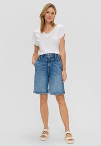 T-shirt bianco a maniche corte con scollatura a V e dettagli annodati, abbinato a pantaloni shorts in denim blu con lunghezza al ginocchio. Footwear casual completa l'outfit.