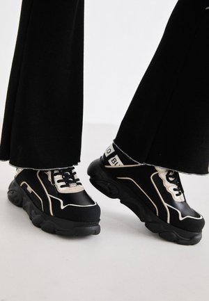 Sneaker neri con accenti bianchi, caratterizzati da una finitura liscia, design a strati, suola testurizzata e lacci prominenti. Silhouette piatta e ampia.