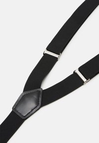Bretelles noires en tissu élastique avec une finition en cuir lisse, dotées de clips en métal pour l'attachement. Design réglable.