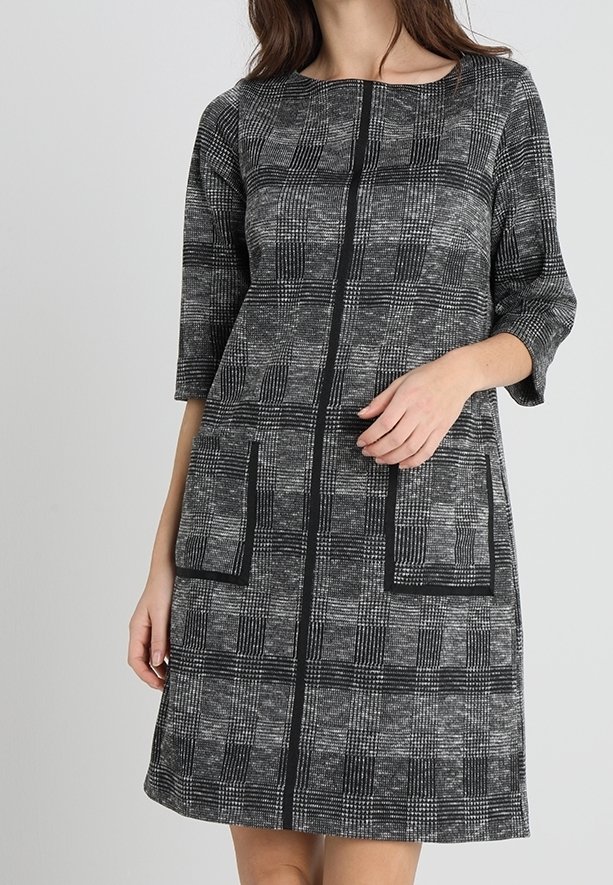 Abito a quadri in bianco e nero con maniche a tre quarti, scollatura rotonda e due tasche frontali. Tessuto strutturato con una forma definita.