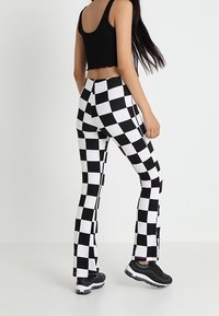 Black and white checkered flared pants with a high waist, smooth fabric texture, and side slits. Worn with a black cropped top and sneakers.