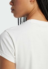 Biała bawełniana koszulka T-shirt z okrągłym dekoltem, krótkimi rękawami i gładką fakturą. Widok z tyłu ukazuje szczegóły przy szyi i szwie na ramieniu.