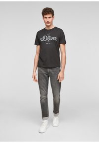 Zwarte katoenen t-shirt met wit "s.Oliver" logo, gecombineerd met grijze spijkerbroek en witte sneakers. De outfit heeft een casual ontwerp en pasvorm.