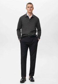Polo de manga larga gris oscuro con una capa inferior de cuello blanco, combinado con pantalones negros a medida y zapatos de cuero negros.