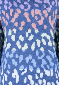 Pull en maille douce avec des taches de léopard dégradées en rose, blanc et bleu clair sur un fond bleu moyen.