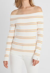 Off-the-shoulder, ribbed sweater with white base and horizontal stripes in orange and gray. Long sleeves and logo detail on sleeve cuff.