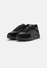 Schwarze Sneakers aus Leder und Wildleder, mit einer strukturierten Oberfläche, runder Zehe und flacher Gummisohle mit einem Profilmuster.