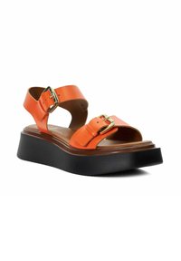 Orange leather platform sandal with wide straps, two gold buckles, and a thick black sole.