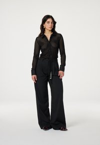 Black striped sheer button-up shirt with long sleeves and tailored high-waisted black trousers featuring a drawstring and subtle embellishments.