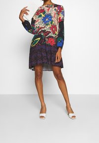 Kleurrijke lange mouw jurk met bloemetjes, met een nauwsluitend bovenstuk en een uitlopende onderkant. Heeft een zwarte achtergrond, ingewikkelde patronen en een gladde textuur.