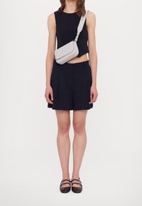 Top corto blu navy e pantaloncini plissettati con borsa a tracolla grigio chiaro. Scarpe con cinturino marrone, punta quadrata e dettaglio a doppio cinturino.