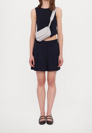 Granatowy krótki top i plisowane szorty z jasno szarą torebką na pasku przez ramię. Brązowe buty z kwadratowym noskiem i podwójnym paskiem.