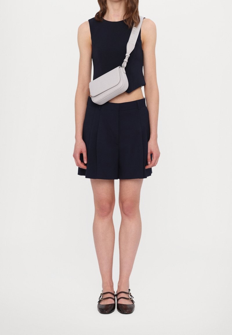 Top corto blu navy e pantaloncini plissettati con borsa a tracolla grigio chiaro. Scarpe con cinturino marrone, punta quadrata e dettaglio a doppio cinturino.