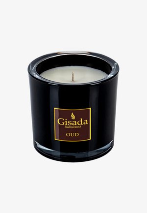 Czarny szklany świecznik z białym woskiem w środku i centralnym knotem. Posiada złotą i brązową etykietę z napisem "Gisada Switzerland OUD."