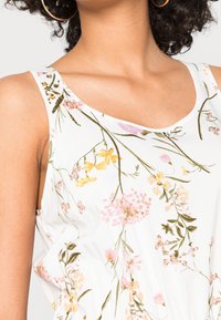 White sleeveless dress featuring a floral pattern with pink, yellow, and green accents, smooth texture, and a curved neckline.