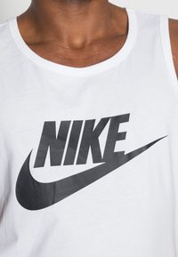 Bela bomba z bombažem z velikim črnim logotipom Nike s pomikom, okroglo ovratnico in gladko, osnovno teksturo.