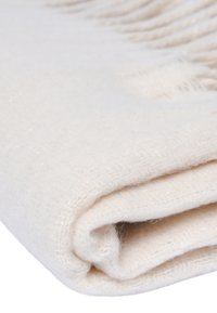 Coperta in lana color crema, texture morbida, presenta una sottile lucentezza, piegata con bordi frangiati, mettendo in risalto il suo aspetto caldo e accogliente.