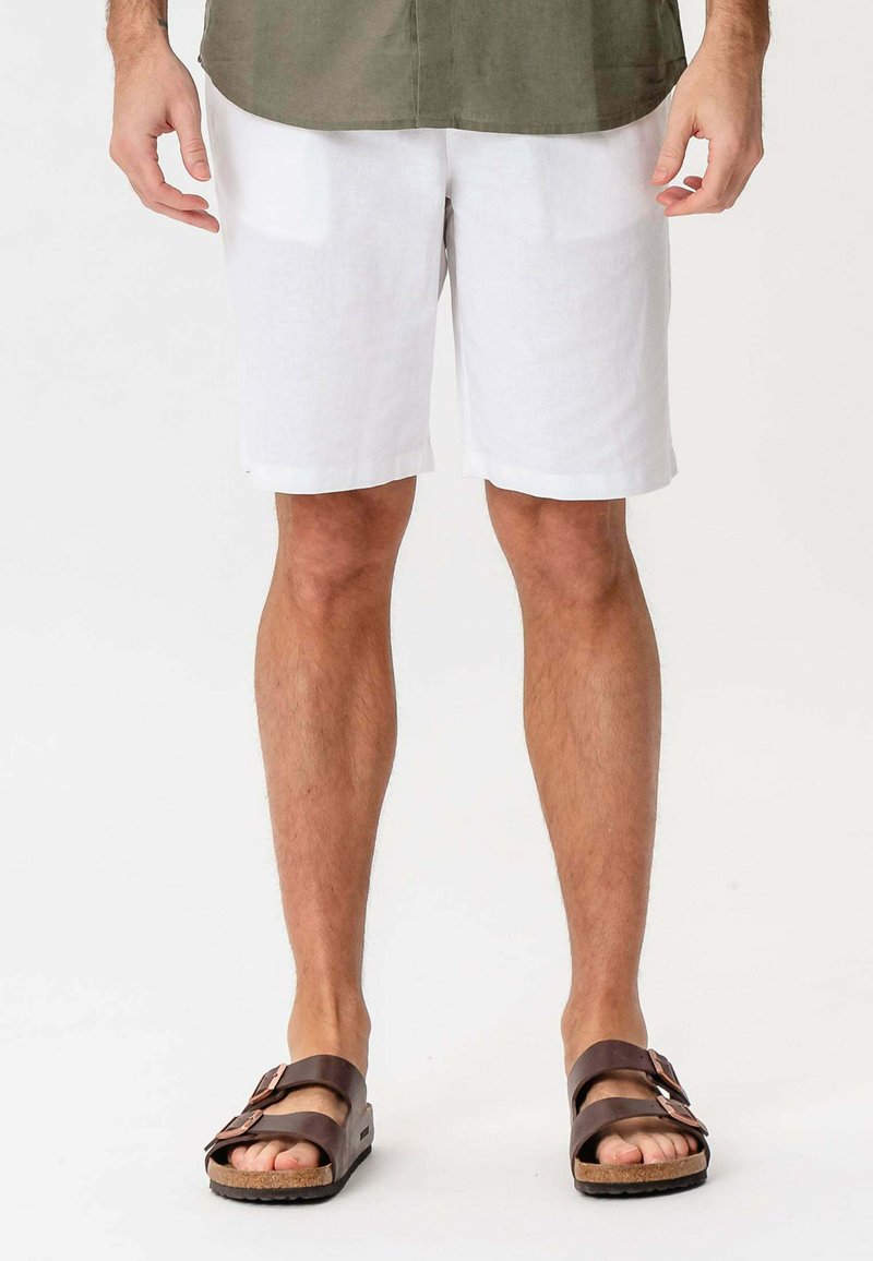 Hvide linnedshorts med en afslappet pasform og opkrøllede kanter. Brune sandaler med to justerbare stropper, tekstureret fodseng og korksål.