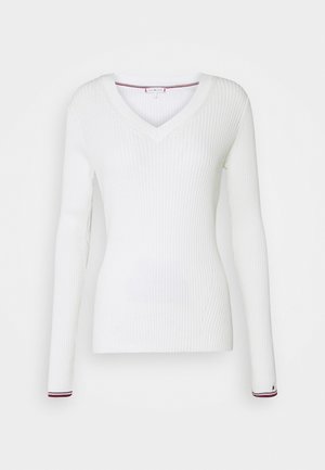 Haut blanc à manches longues côtelé avec un col en V. Présente une coupe ajustée et un détail coloré à l'ourlet des manches. Confectionné dans un matériau extensible.