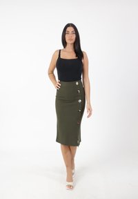Top in cotone nero fitted con spalline sottili, abbinato a una gonna a matita verde oliva lunga fino al ginocchio, caratterizzata da uno spacco laterale e grandi bottoni argentati.