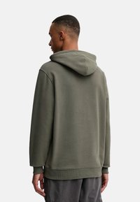 Sudadera verde oliva hecha de tejido suave, con un bolsillo canguro y capucha con cordón. Ajuste cómodo y relajado con puños de canalé.