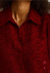 Rotes Hemd mit Knopfleiste, das strukturierte Blumenmuster, einen Kragen und ein transparentes Gewebe mit geschichteten Paneeldetails aufweist.