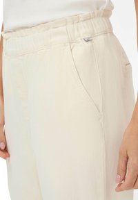 Lichtbeige elastische broek met tailleband en zijzakken, met een gladde textuur en een ontspannen pasvorm. Inclusief een klein merketiket op de tailleband.