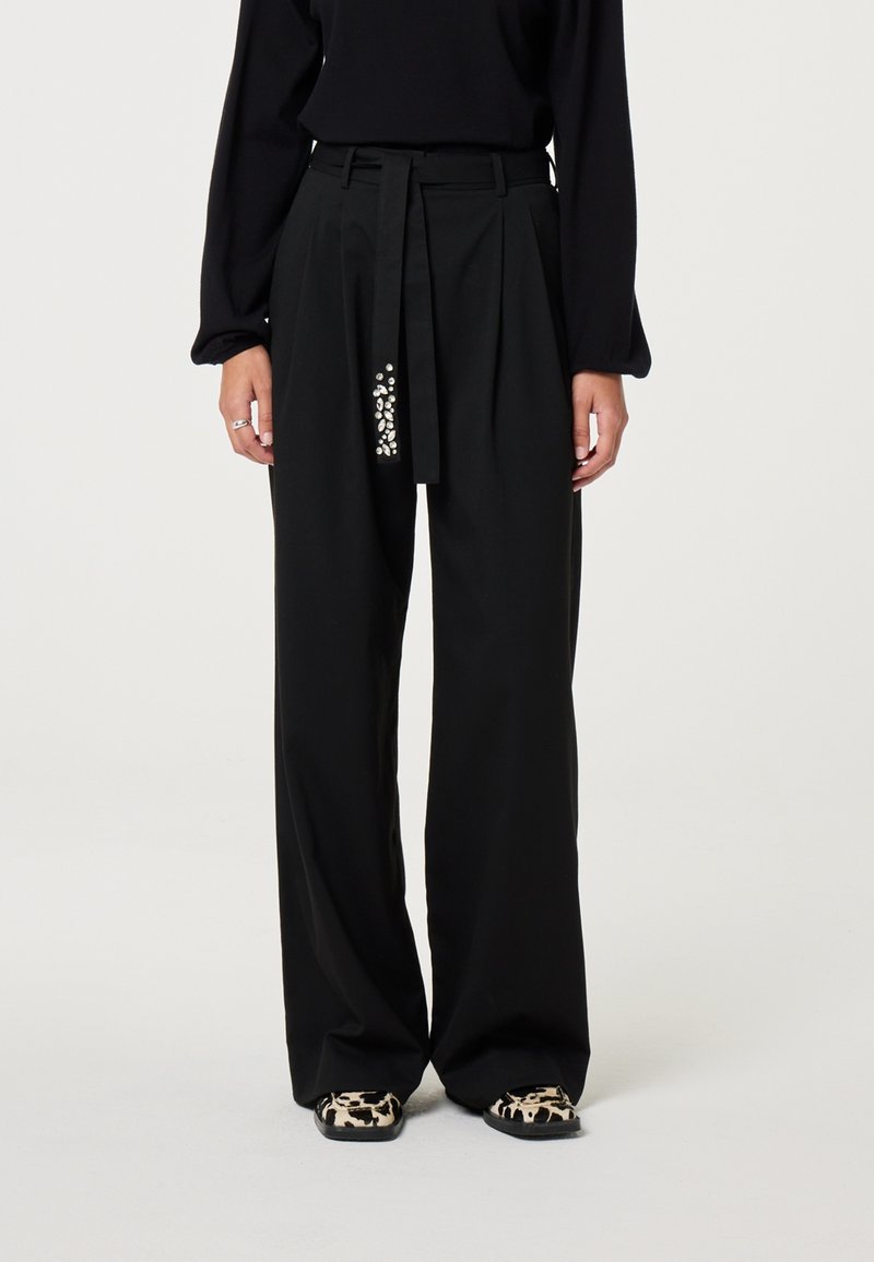 Zwarte wijde broek met een ceintuur in de taille, met een decoratief, gewatteerd detail aan één kant en een gladde stofafwerking.