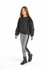 Svart sweatshirt med paljetter på axlarna, tillsammans med svarta och vita houndstooth leggings med sidofickor, och svarta kängor.