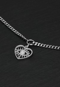 Silberne Kettenhalskette mit einem Herzanhänger mit geometrischem Design und einem zentralen klaren Edelstein. Texturierte Metalloberfläche.