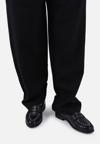 Black leather loafers with studded accents and a smooth finish, paired with loose black pants, showcasing a tailored, contemporary design.