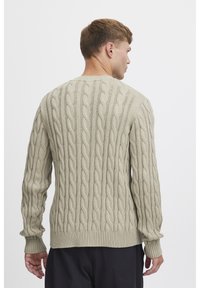 Pull en maille torsadée de couleur beige clair, avec un motif texturé, des poignets et un ourlet côtelés, et un col rond. Vue arrière présentée.