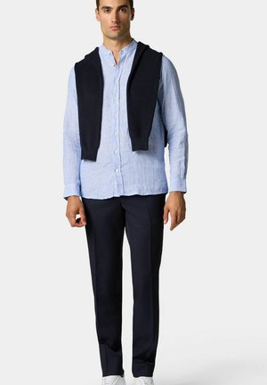 Blauwe gestreepte button-up shirt, marineblauwe trui over de schouders, marineblauwe broek en witte sneakers. Glad materiaal, op maat gemaakt.