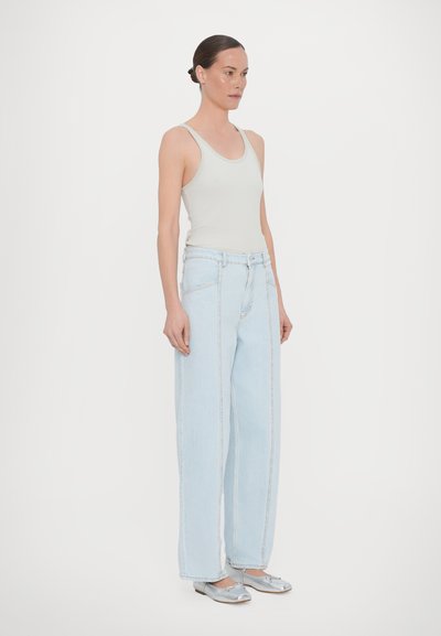 Lys grå tanktopp, høytlivede lyseblå vide jeans og blanke sølvflats. Glatt stoff med subtile sømdetaljer.