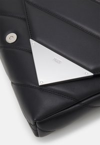 Róg czarnej pikowanej torebki skórzanej z srebrną, trójkątną blaszką logotypu wyrytą napisem "DKNY" oraz okrągłym zapięciem magnetycznym.