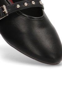 Zapato de cuero negro con punta afilada, que presenta una correa ancha adornada con tachuelas plateadas y una hebilla en el lado. Textura suave.