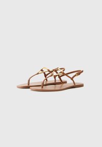 Sandali piatti marroni con sottili cinturini e dettagli metallici dorati. Presentano una superficie liscia e un design minimalista.