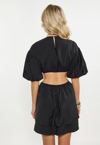 Schwarzes Crop-Top mit puffärmel und runder Ausschnitt, kombiniert mit einem fließenden schwarzen Rock mit elastischem Bund und geschichteter Saumverarbeitung.