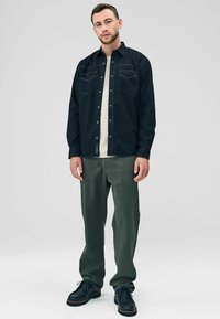 Dark blue denim button-up shirt with two chest pockets, cream t-shirt underneath, olive green pants, and black lace-up shoes.