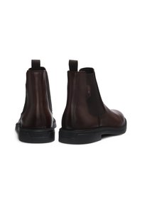 Botine Chelsea din piele maro cu panouri elastice laterale, curele de tragere și talpă din cauciuc negru. Prezintă o textură netedă și detalii subtile de cusătură.
