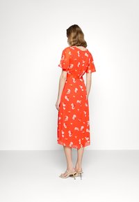 Robe midi rouge à fleurs avec manches courtes volantées, taille cintrée et ourlet fluide. Présente des fleurs rose clair sur un fond éclatant.