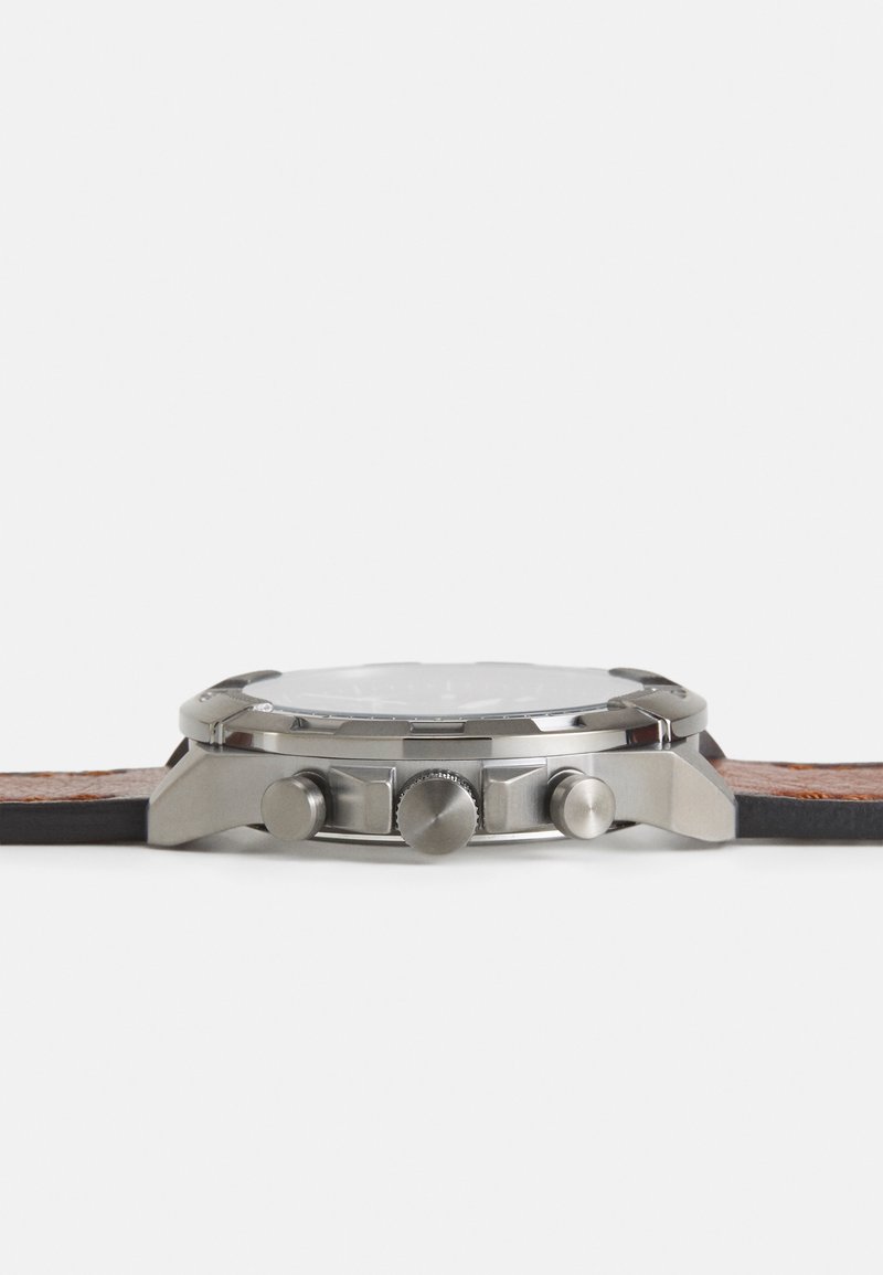 Montre en métal argenté avec un cadran rond, un cadran blanc texturé et un bracelet en cuir marron. Ses caractéristiques comprennent trois poussoirs et une couronne texturée.