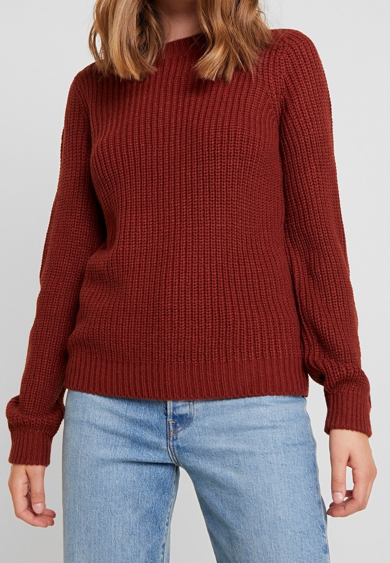 Pull en maille bordeaux à manches longues, texture côtelée et col rond, associé à un jean bleu clair.
